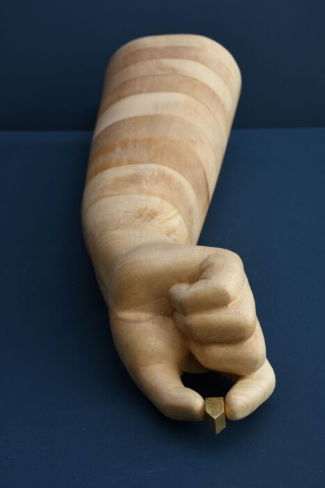 Wooden sculpture of big hand holding a small house lying down